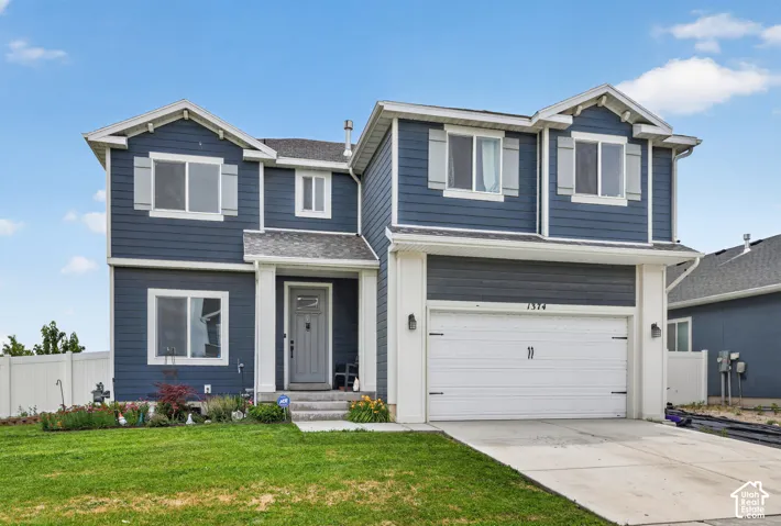 Blue siding exterior with white trim, featuring a two-car garage, concrete driveway, and front entryway with a covered porch