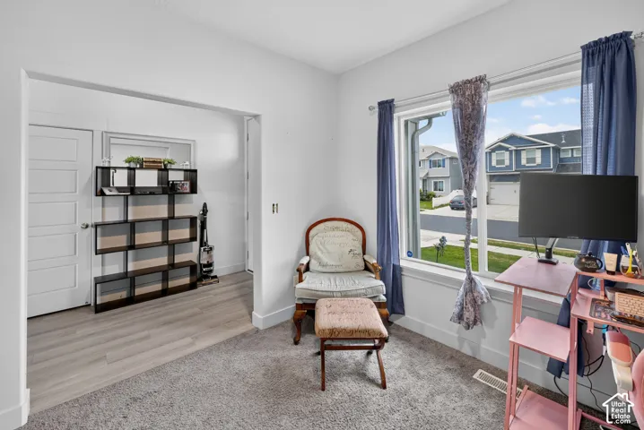 Room featuring a large window, light-toned walls, and a combination of grey carpet and wood-finish flooring