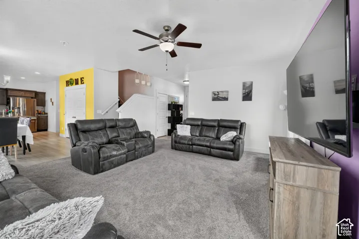 Open-concept living space featuring light gray carpeting, a ceiling fan with integrated lighting, and white walls