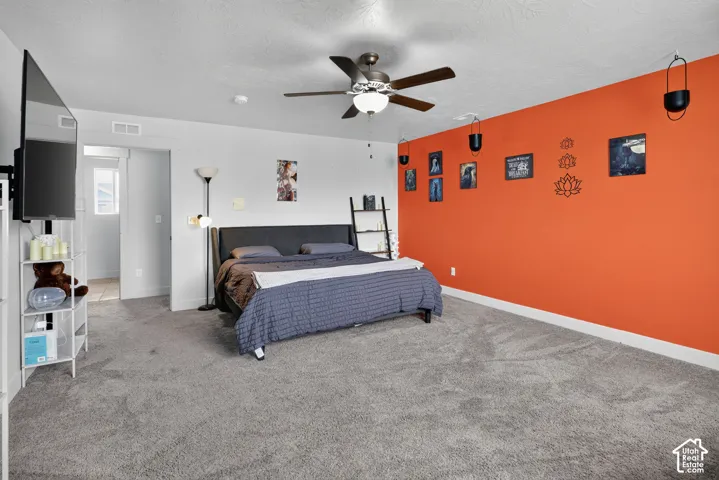 Carpeted bedroom featuring an accent wall, ceiling fan with integrated lighting, and white baseboards
