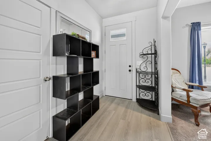 Entryway featuring a white paneled door with decorative glass insert, light wood-finish flooring, and white trim