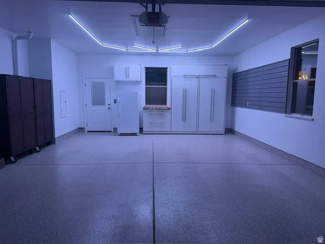 Spacious garage featuring epoxy flooring, built-in white cabinetry, a built-in workbench with a wood-finish countertop, a dedicated storage wall system, and recessed overhead lighting
