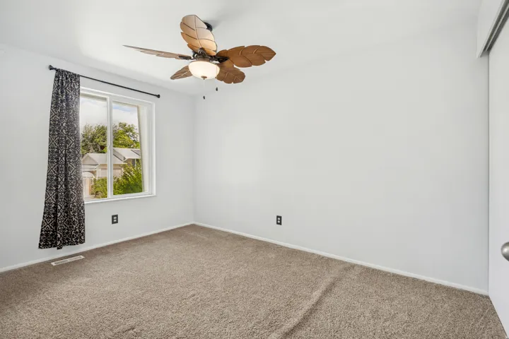 Bright room featuring neutral carpet flooring, a window with exterior views, and a ceiling fan with leaf-shaped blades