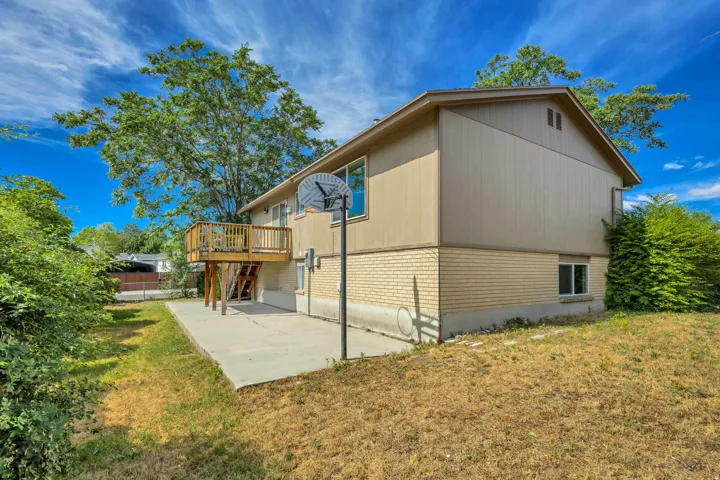 Two-story exterior with a wood deck, concrete patio, and brick-bottom siding