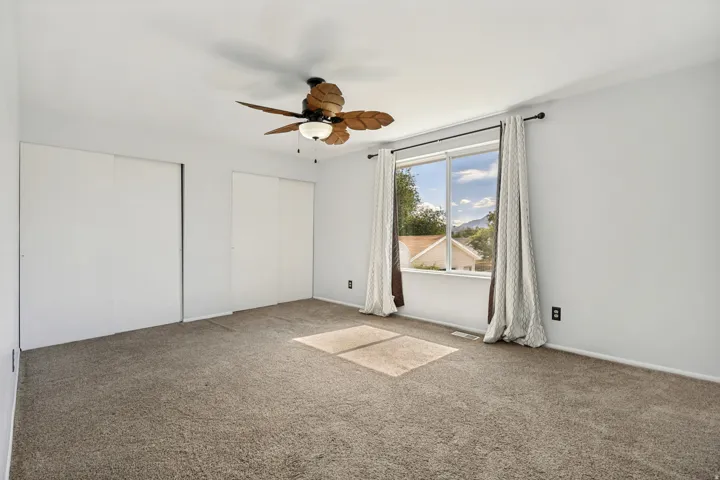 Light-filled room featuring neutral wall tones, plush carpeting, and a tropical-inspired ceiling fan