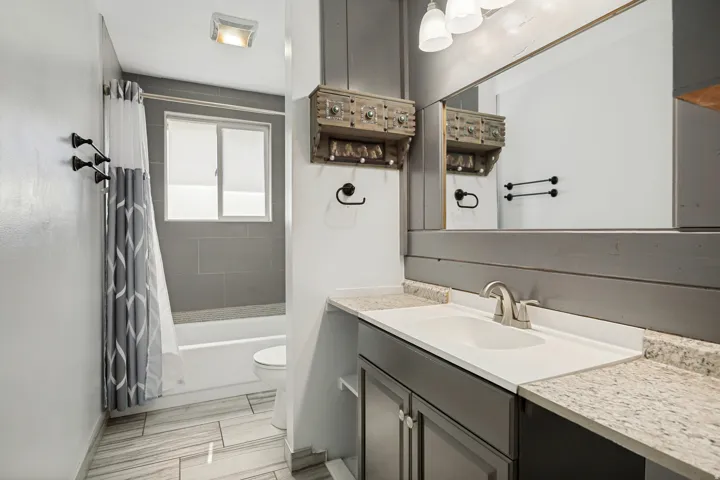 Bathroom featuring a white bathtub, gray tiled shower surround, and a white vanity with an integrated sink