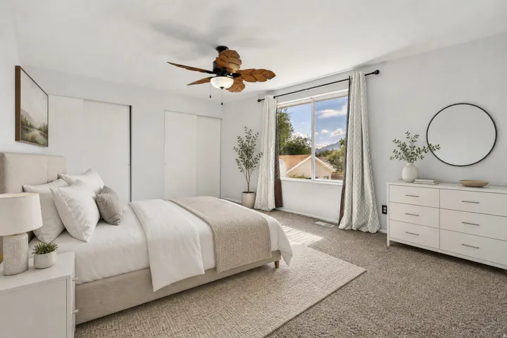Spacious primary bedroom featuring light-toned walls, plush carpet flooring, double closets and a ceiling fan with decorative wooden blades