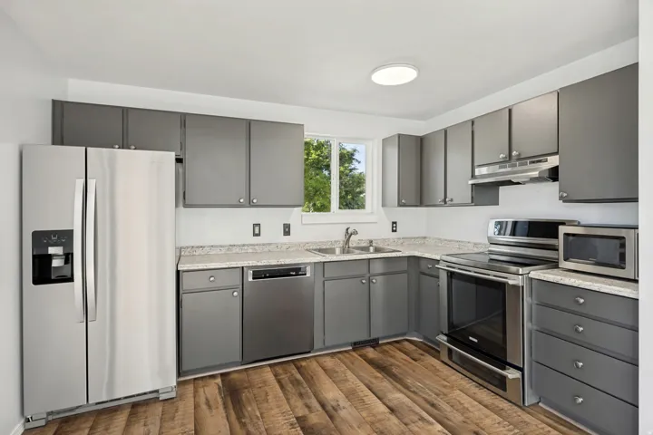 Open-concept kitchen featuring wood-finish flooring, shaker-style cabinetry, stainless steel appliances, speckled countertops, and a double basin sink