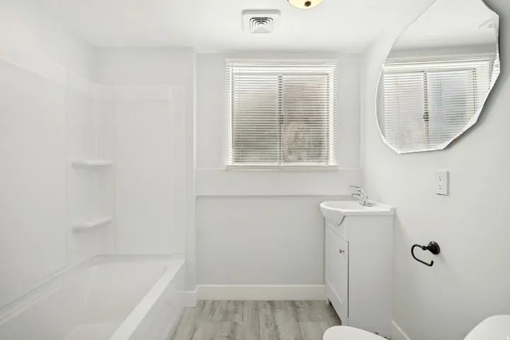 Bathroom featuring a bathtub with an integrated shower, white vanity with a basin sink, and a window with blinds