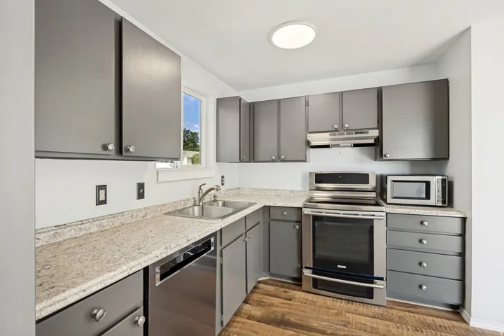 Kitchen featuring grey cabinetry, light-toned countertops, stainless steel appliances, a double basin sink, and wood-finish flooring