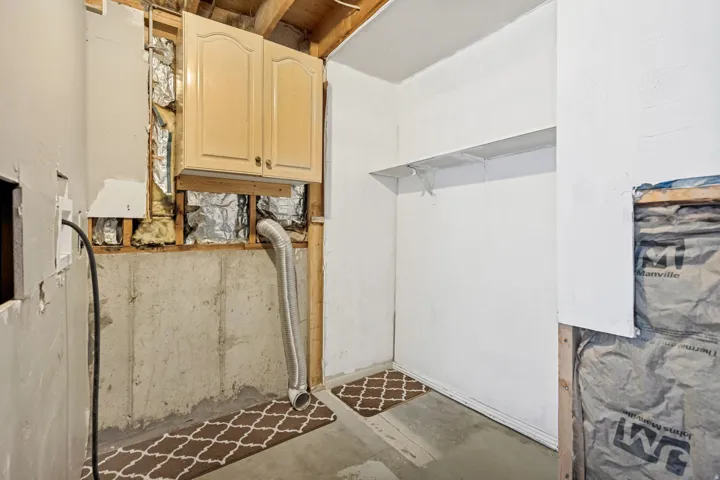 Unfinished room featuring a concrete foundation wall, exposed wood framing, and an overhead cabinet with arched panel doors