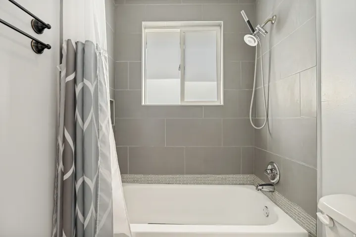 Bathroom featuring a white tub, light gray subway tile surround, mosaic accent tile, and a window for natural light