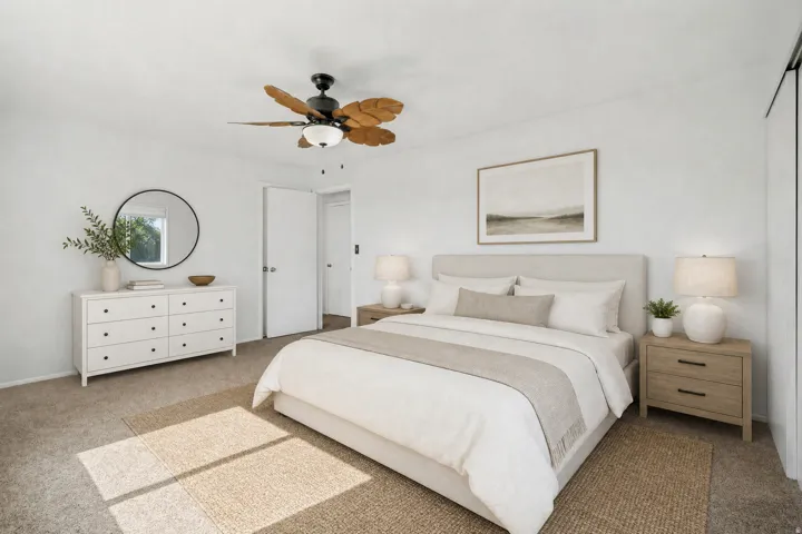 Carpeted bedroom featuring a ceiling fan with light fixture, white walls, and a window with a circular mirror