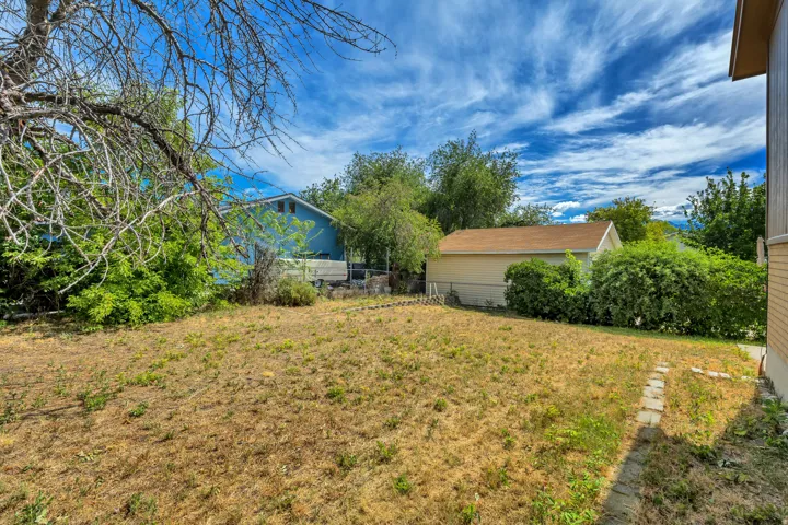 Spacious backyard area featuring a detached structure with a pitched roof, mature trees, and a stone-paver walkway