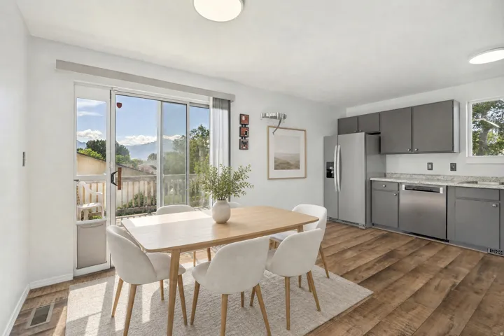 Open-concept dining area featuring wood-finish flooring, sliding glass doors to outdoor space, and a bright kitchen with grey cabinetry, light countertops, and stainless steel appliances