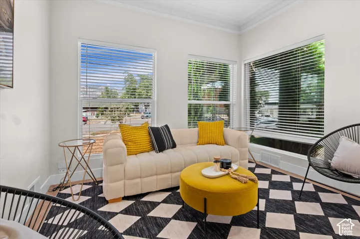 Bright living space featuring multiple windows with blinds, crown molding, and wood-finish flooring