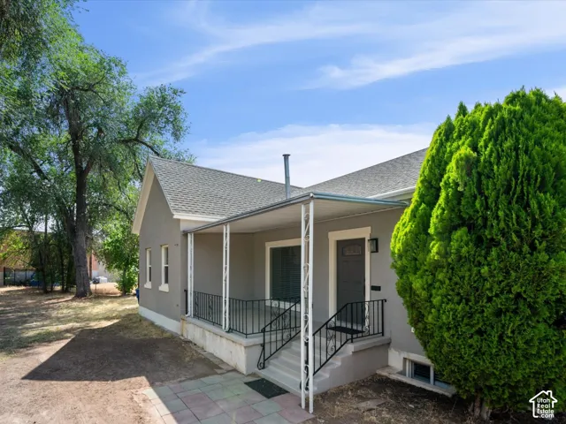 Exterior featuring a covered porch with white columns and black railings, a gray facade, and a dark entry door