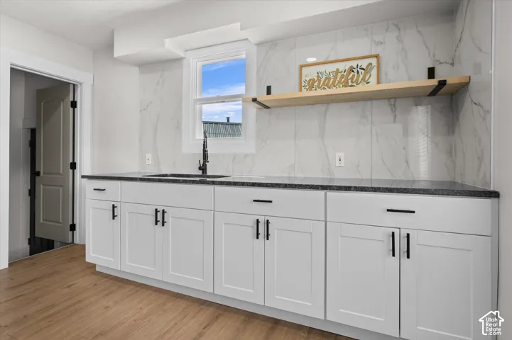 White shaker cabinetry with dark hardware, dark speckled countertops, and a white marble-look tile backsplash
