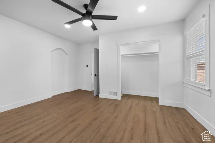 Spacious room featuring wood-finish flooring, white walls, and a modern black ceiling fan with integrated lighting