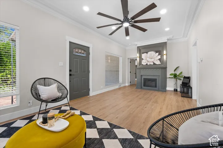 Spacious living area featuring wood-finish flooring, a contemporary ceiling fan with integrated lighting, and crown molding
