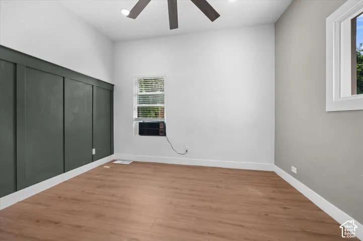 Room featuring wood-finish flooring, a contemporary ceiling fan, and a prominent dark accent wall with vertical paneling