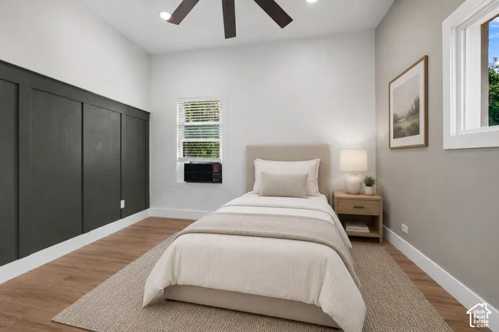 Bedroom featuring a decorative board and batten accent wall, wood-finish flooring, and a ceiling fan with integrated lighting