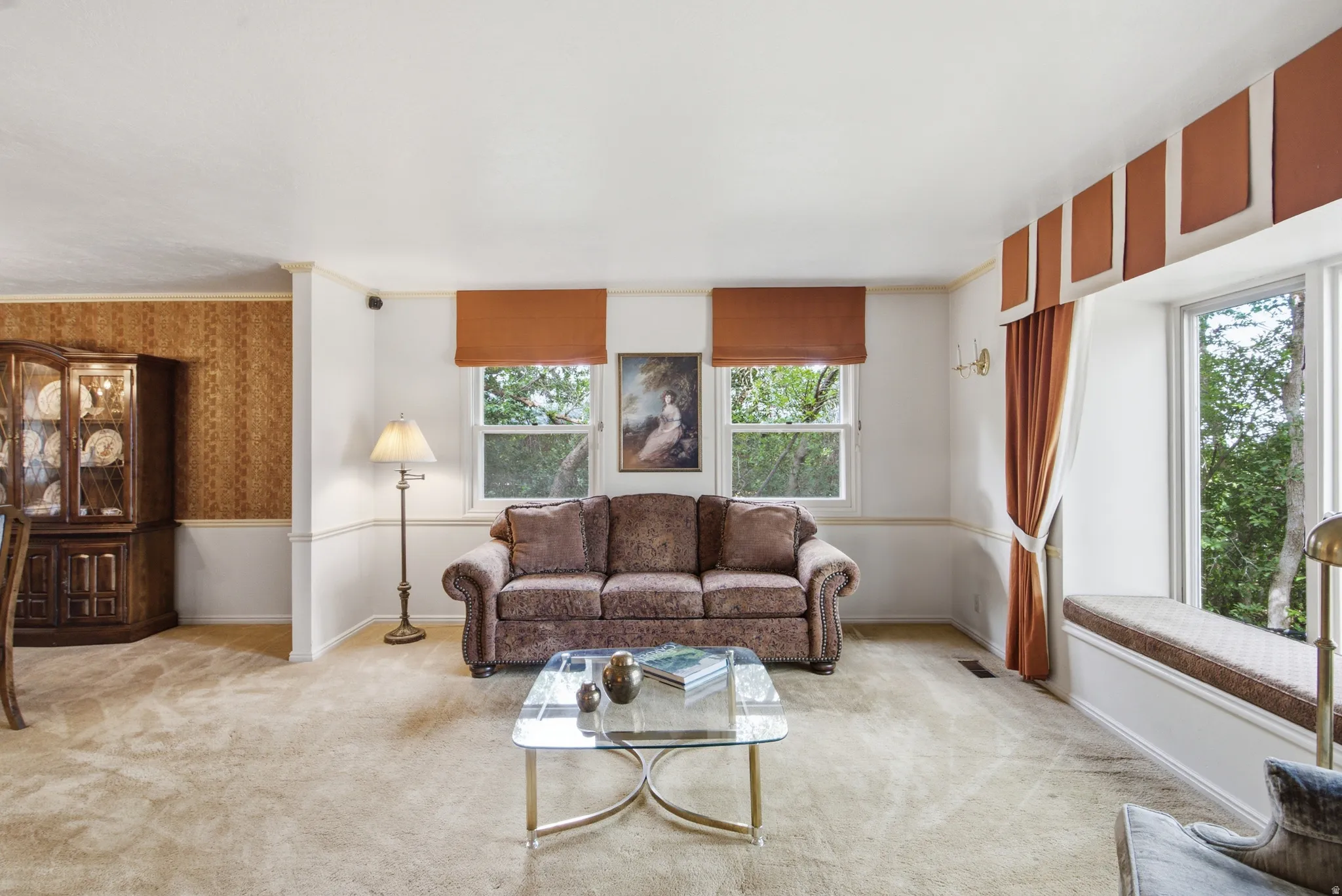 Carpeted living area featuring a built-in window bench, two double-hung windows, and white wainscoting