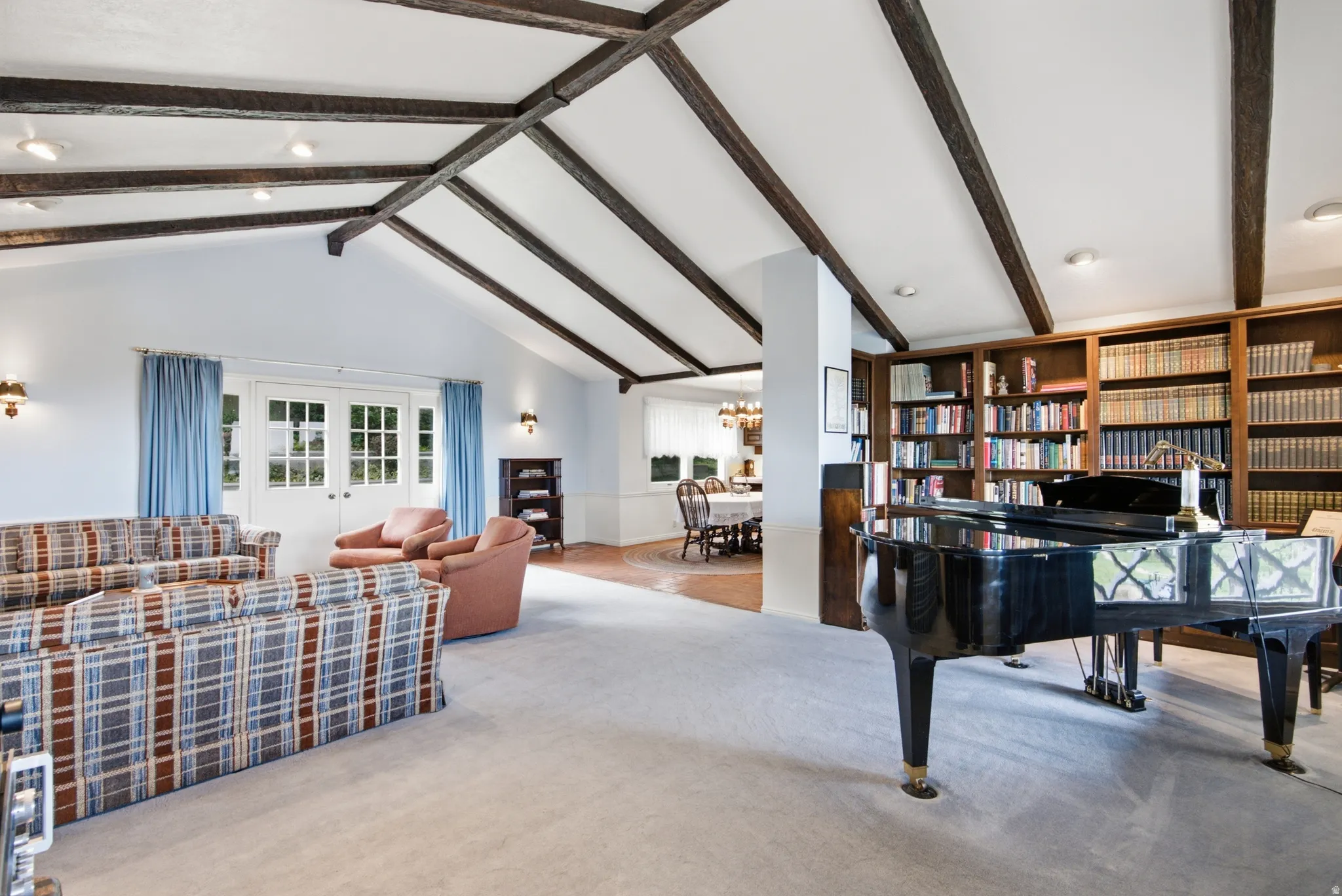 Spacious living area featuring a vaulted ceiling with exposed wood beams, recessed lighting, and wall-mounted sconces