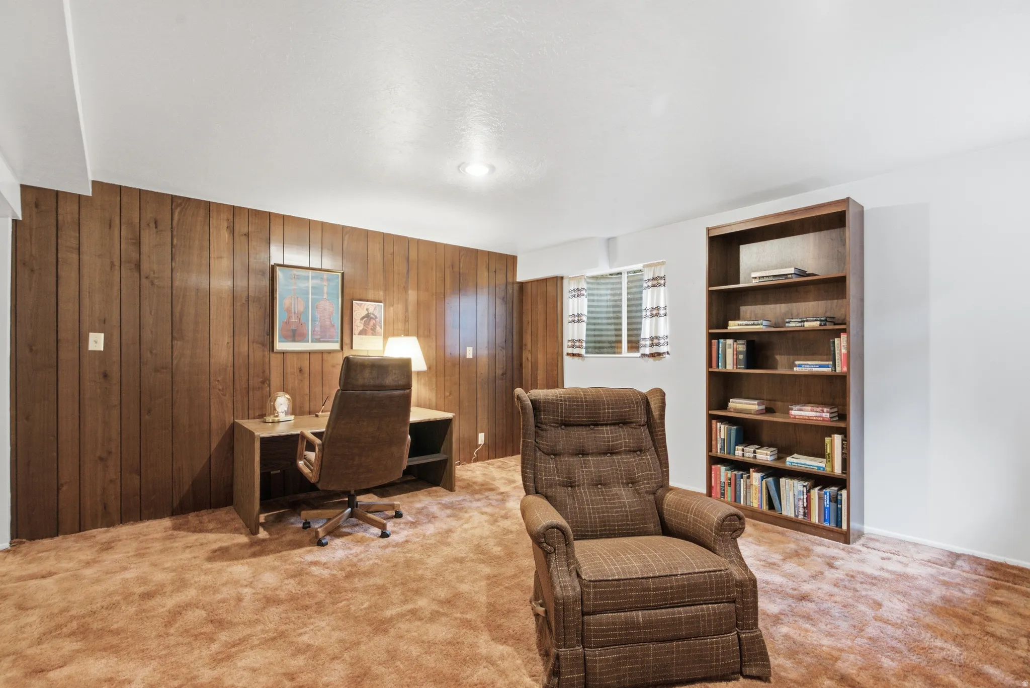 Room featuring wood paneling accent wall, white painted walls, and brown carpeting