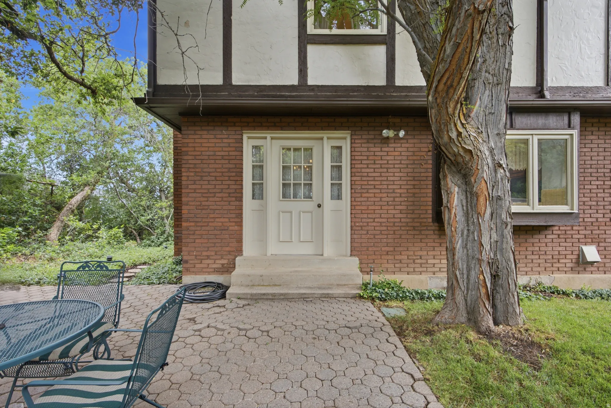 Brick exterior featuring a paneled entry door with sidelights and transom window, a paved patio, and mature trees