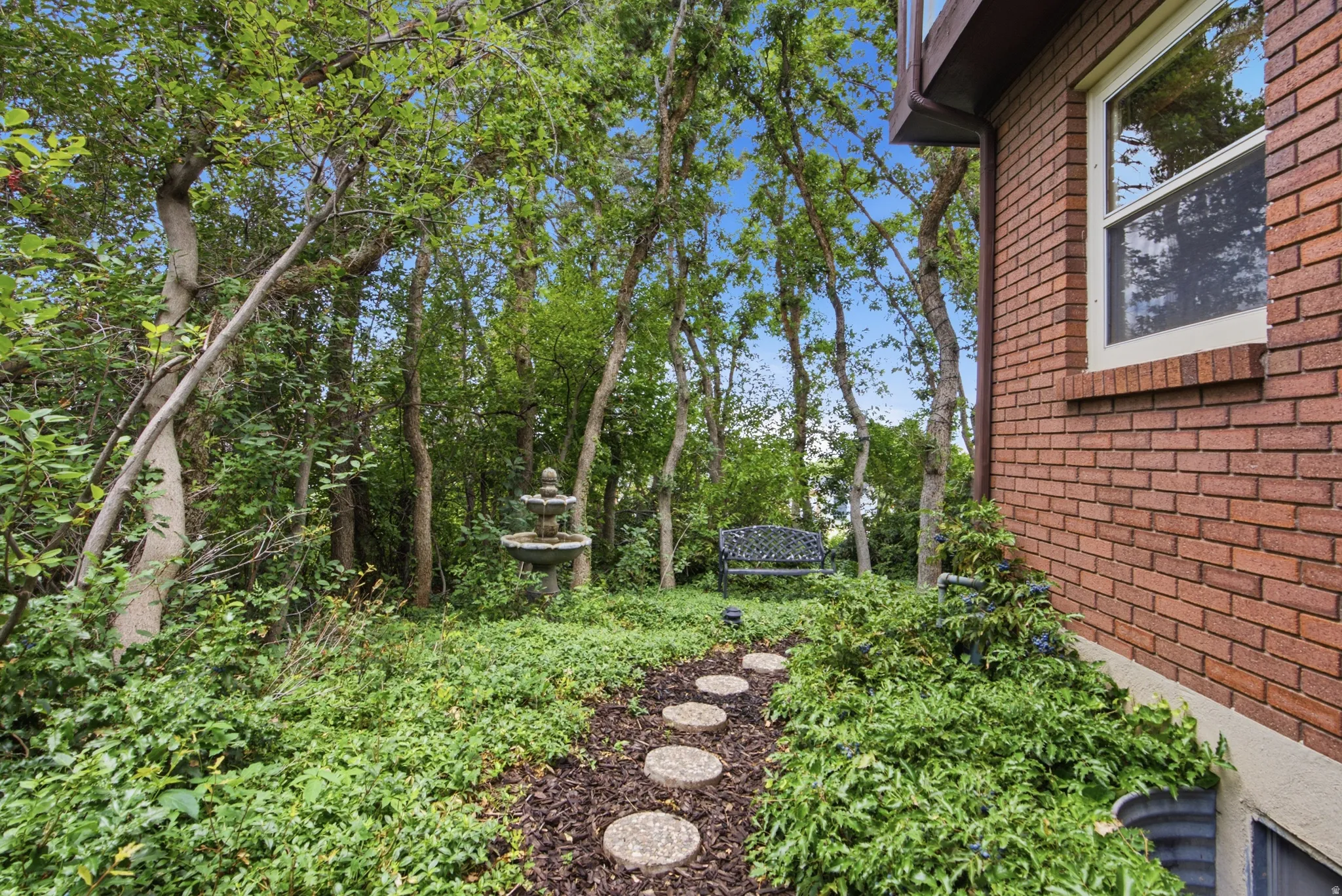 Established landscaping featuring mature trees, a multi-tiered fountain, and a stepping stone path