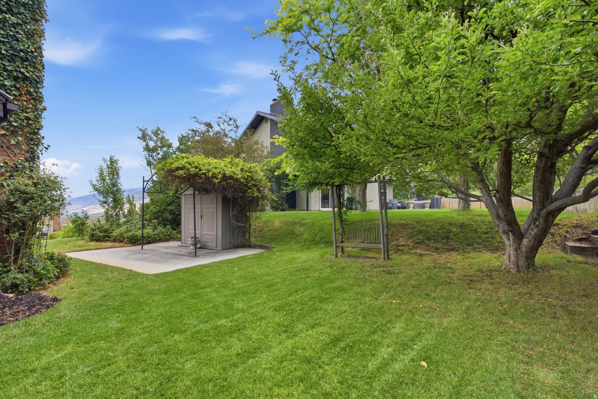 Expansive terraced yard featuring established trees, a storage shed on a concrete pad, and a sloped lawn