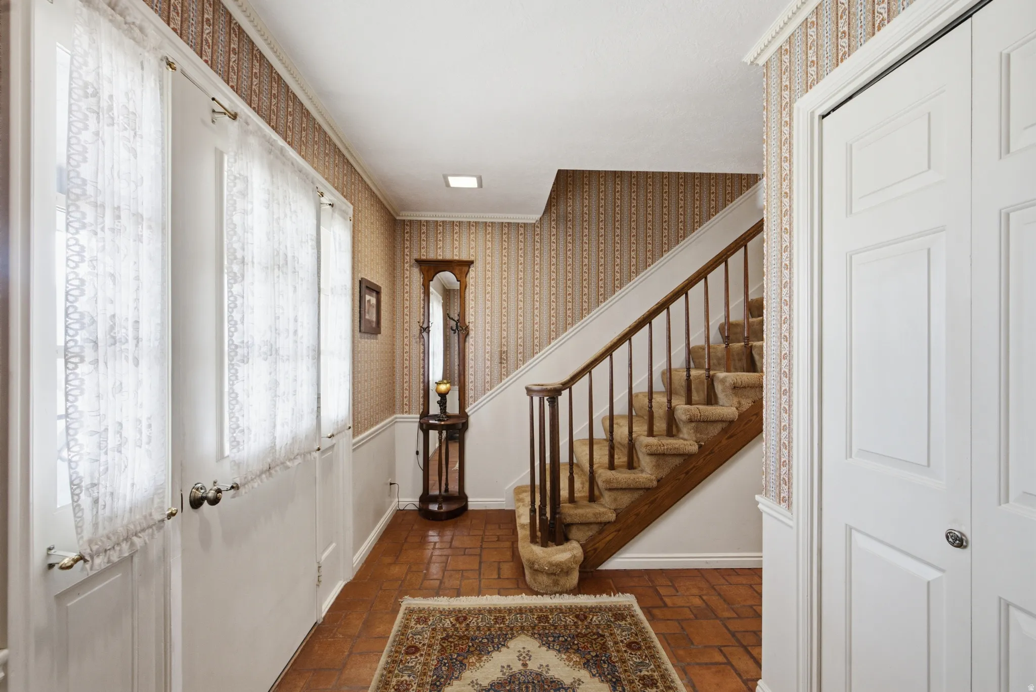 Entryway featuring terracotta-style tile flooring and a carpeted staircase with wood handrails