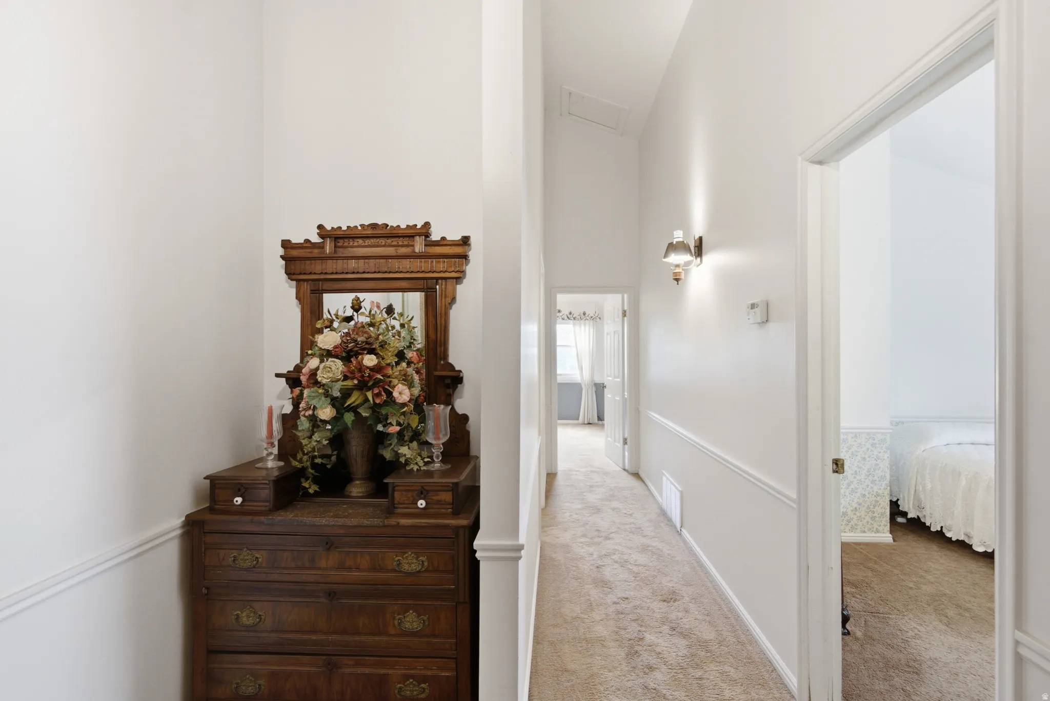 Carpeted hallway with white walls, chair rail molding, and wall-mounted lighting