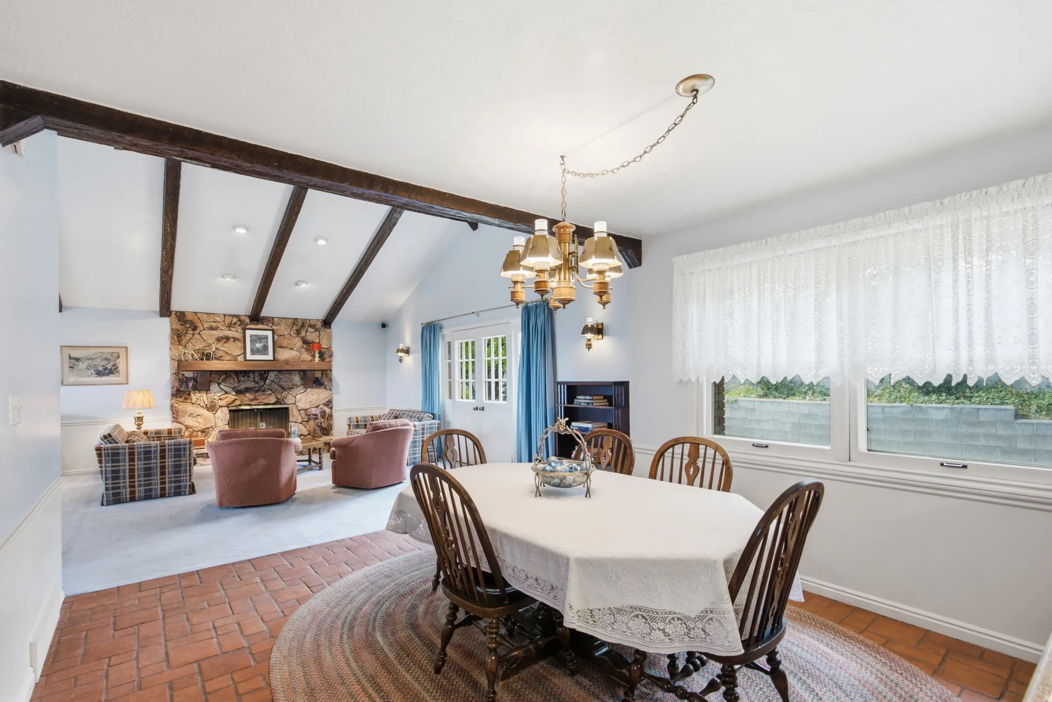 Open-concept interior featuring a brick paver floor entry, a dining area with a brass chandelier, and a living area with a vaulted ceiling
