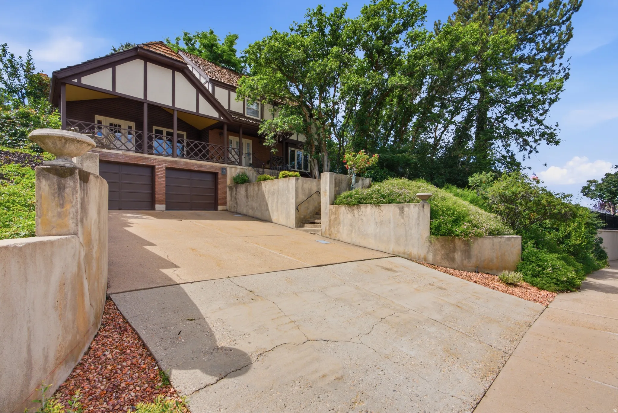 Multi-level home featuring a two-car garage with brown doors, a second-story balcony with brown railings, and a concrete driveway