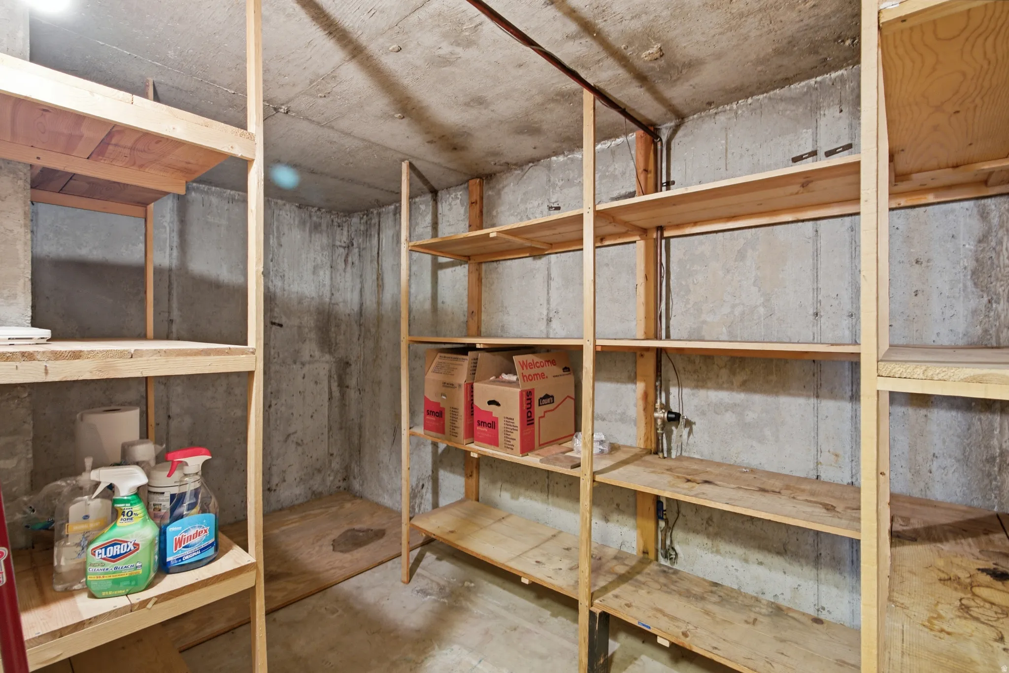 Basement storage area featuring extensive built-in wooden shelving and concrete walls and flooring