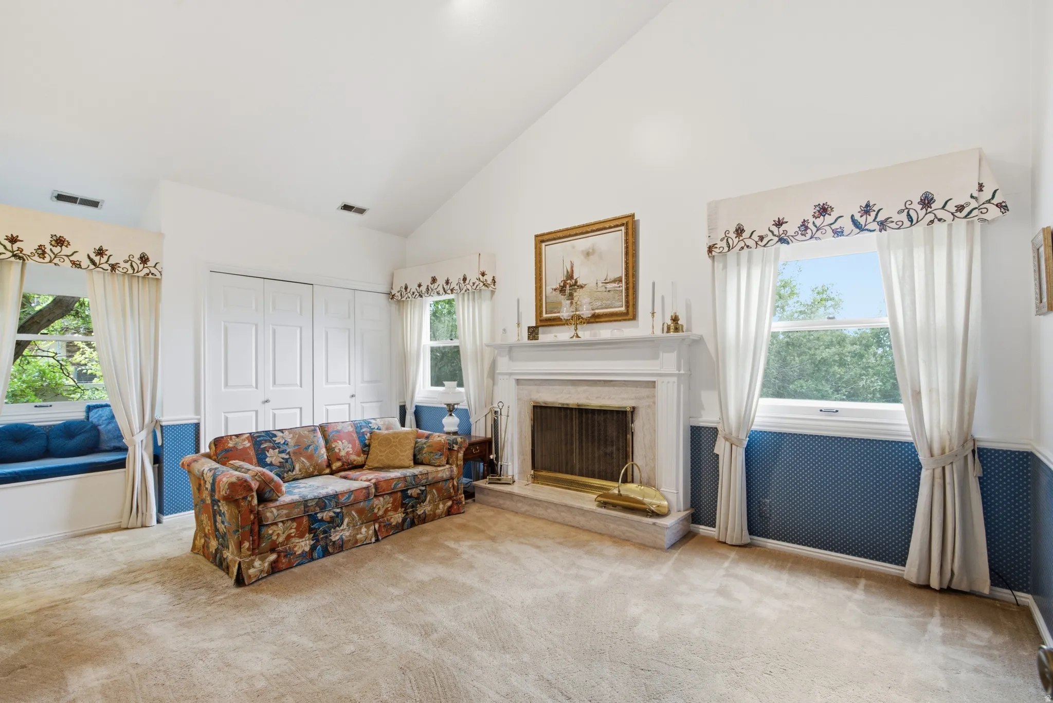 Spacious room featuring a vaulted ceiling, a fireplace with a white mantel, and light-colored carpeting