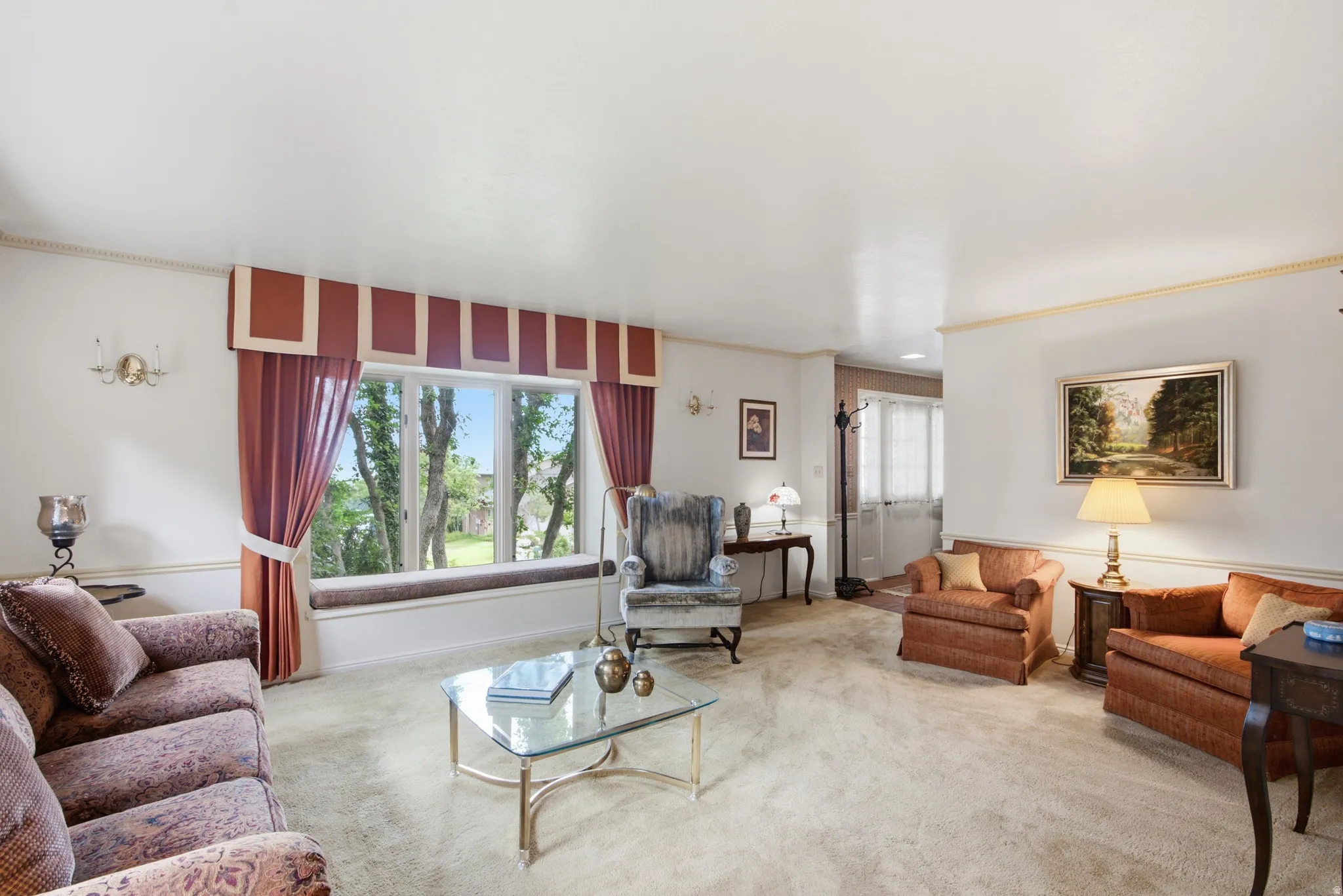 Living area featuring wall-to-wall carpeting, a large bay window with a built-in window seat, crown molding, and wall sconces