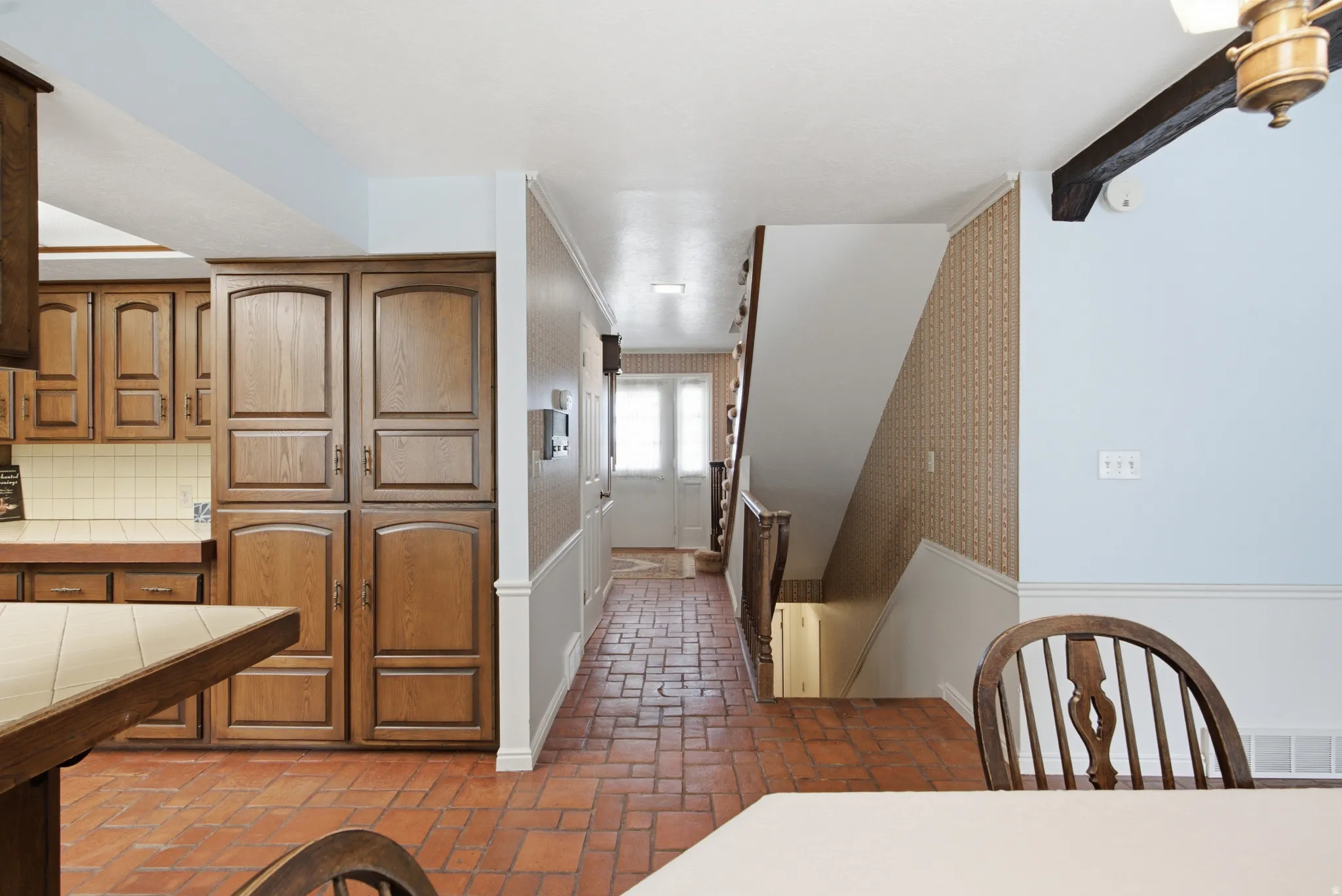 Hardwood cabinetry with ample storage, tile countertops, brick-finish flooring, and a traditional staircase with wood railing