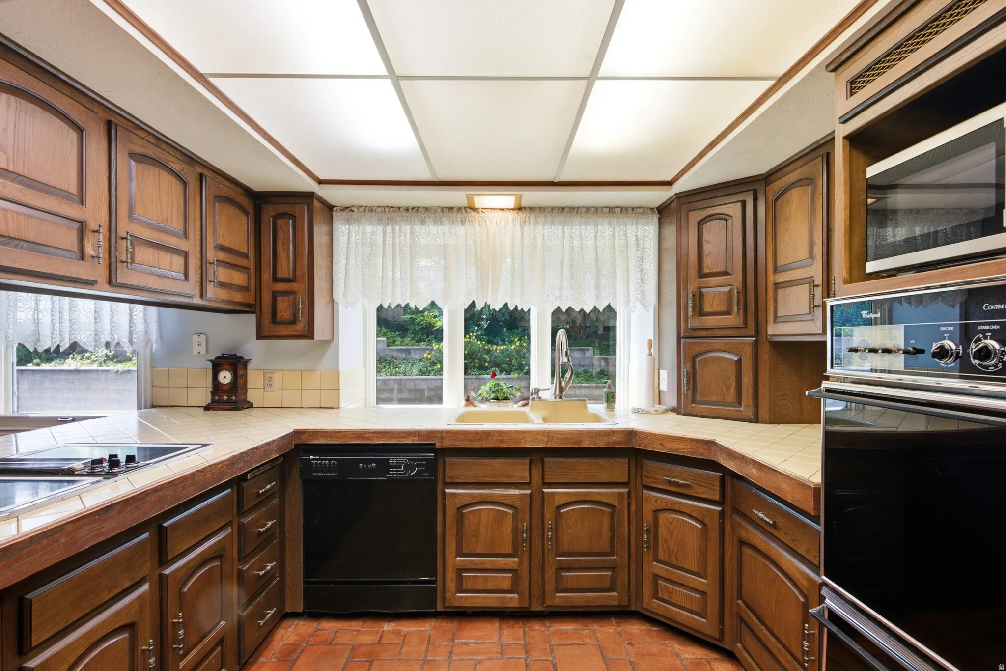 Kitchen featuring abundant wood cabinetry, integrated oven, built-in microwave, tile countertops, and terracotta tile flooring