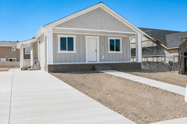 New construction residence featuring a light gray exterior with board and batten siding, shake shingle gables, a covered front porch, and a concrete driveway