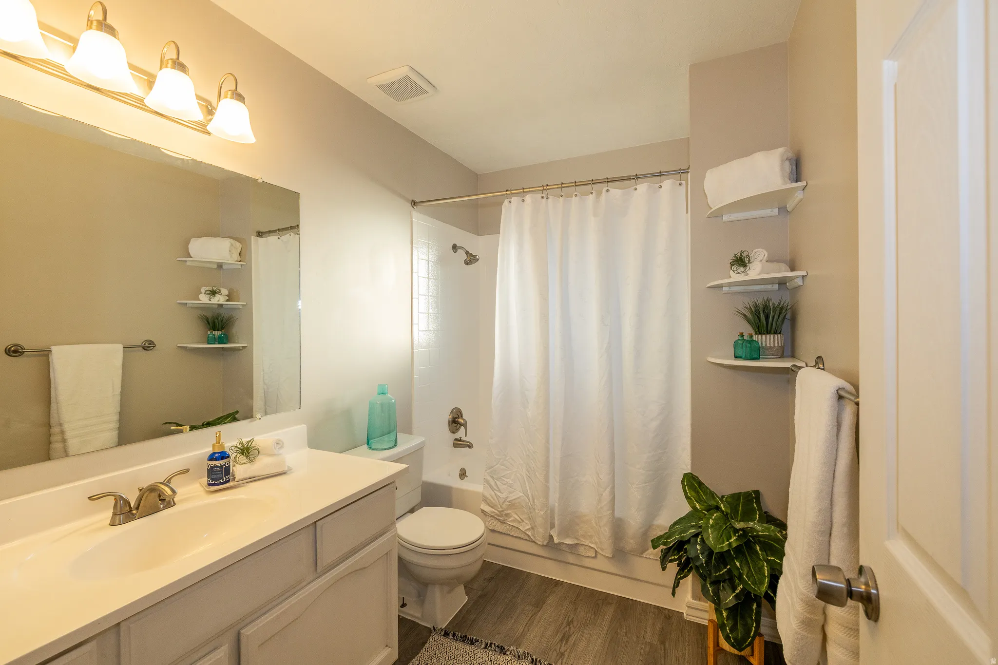 Bathroom featuring a light-colored vanity with an integrated sink, brushed nickel faucet, a large wall-mounted mirror, and a three-bulb vanity light fixture