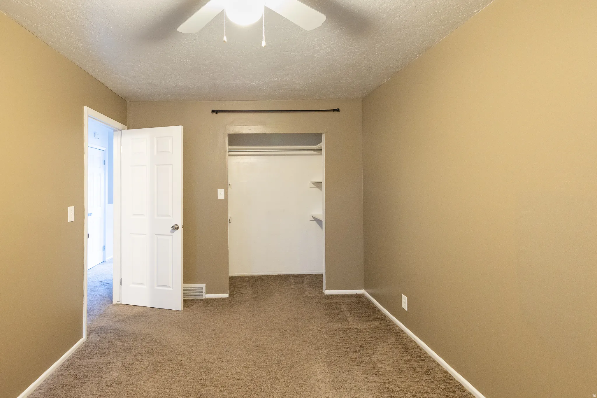 Carpeted room with neutral wall tones, featuring a ceiling fan with integrated lighting, a built-in closet with shelving, and white trim