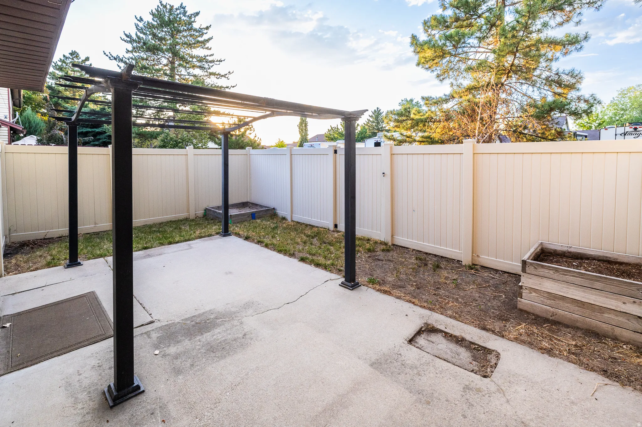 Concrete patio featuring a black metal pergola, surrounded by a light-colored privacy fence