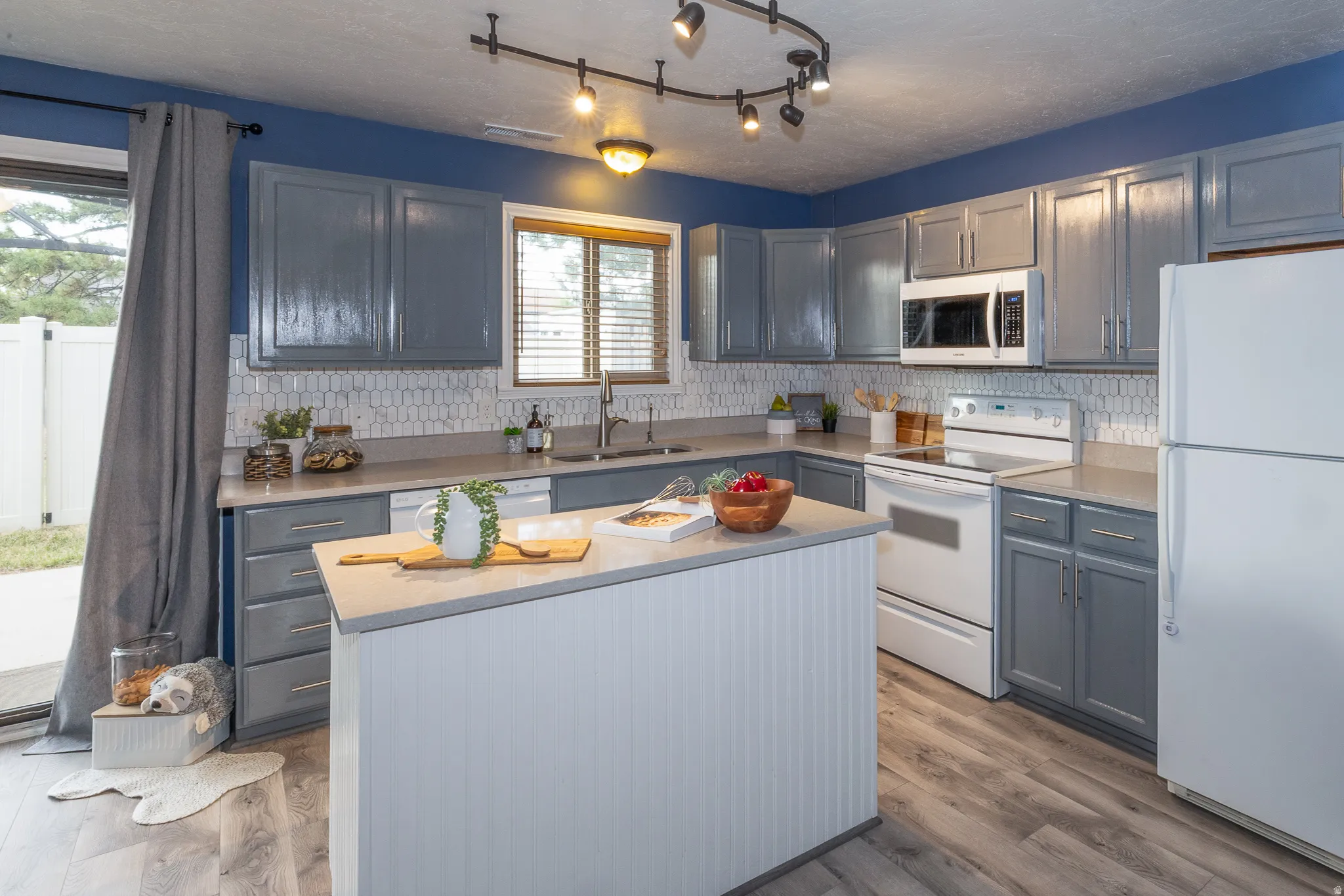 Well-appointed kitchen featuring white appliances, gray cabinetry, and light wood-finish flooring