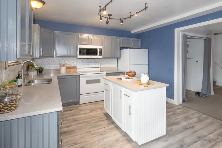 Modern kitchen featuring gray cabinetry, a white tile backsplash, light countertops, wood-finish flooring, and a central white island