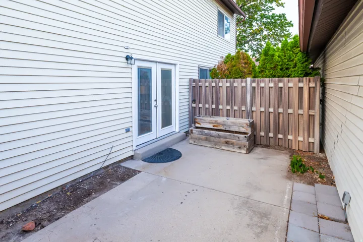 Patio area featuring white vinyl siding, double French doors with glass panels, a concrete patio surface, a wood privacy fence, and integrated wooden planters
