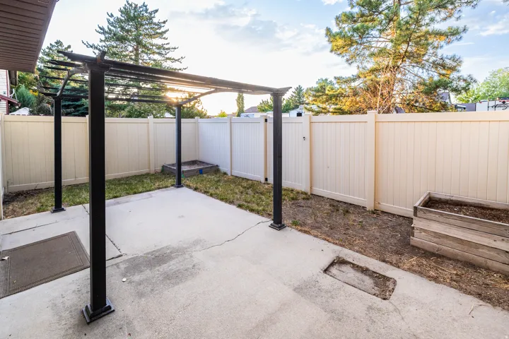 Concrete patio featuring a black metal pergola, surrounded by a light-colored privacy fence