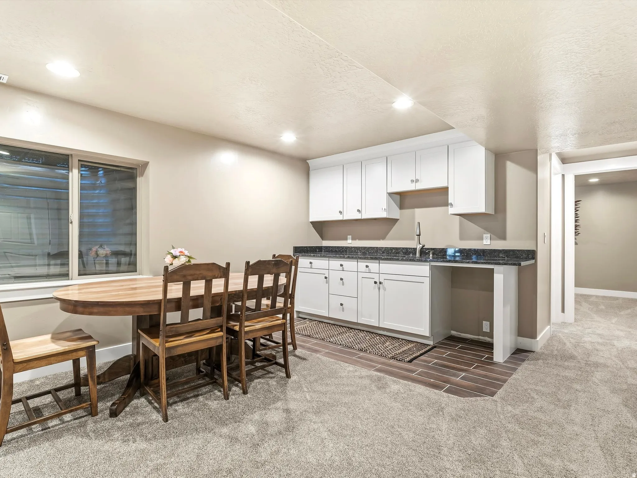 Lower-level entertainment space featuring a wet bar with white cabinetry and dark countertops